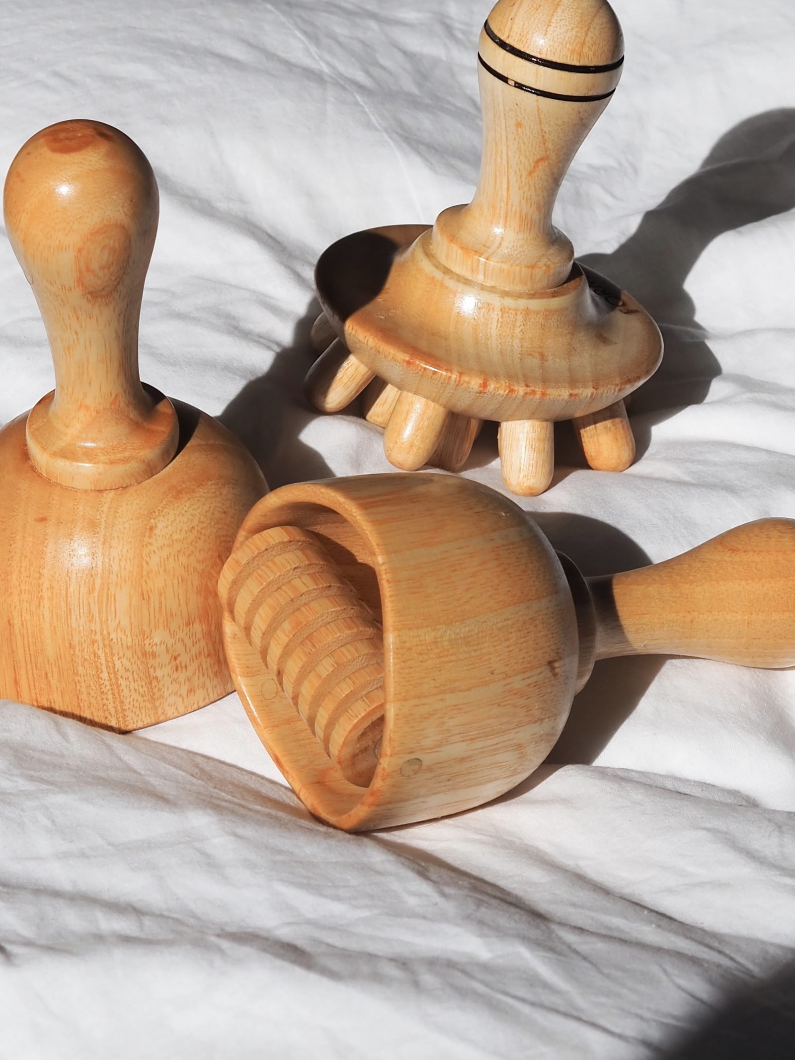 Outils de madérothérapie en bois — ventouse, rouleau et masseur — posés sur un drap blanc au soleil